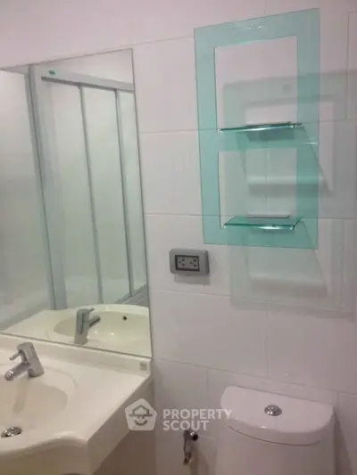 Modern bathroom with sleek fixtures and glass shelving in a contemporary apartment.