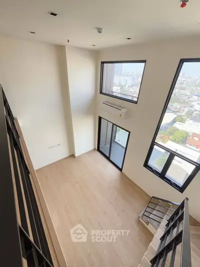 Spacious modern loft with large windows and city view, featuring sleek staircase and wooden flooring.