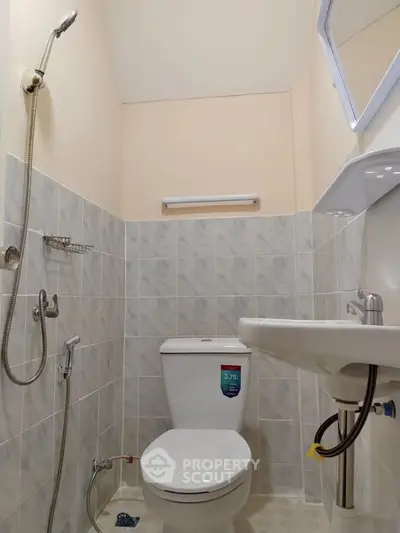 Compact bathroom with modern fixtures and neutral tiles, featuring a toilet, sink, and showerhead.