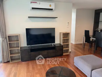 Modern living room with sleek furniture and hardwood floors, featuring a large TV and air conditioning.