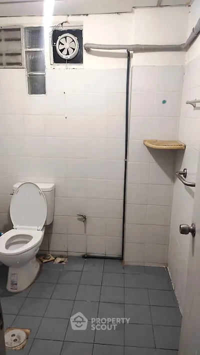Simple bathroom with white tiles and basic fixtures, featuring a toilet and ventilation fan.