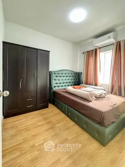 Cozy bedroom with elegant green bed and wooden wardrobe, perfect for relaxation.