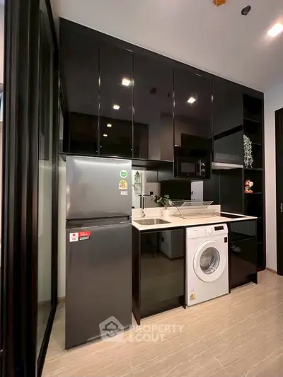 Modern kitchen with sleek black cabinets, stainless steel fridge, and built-in washing machine.