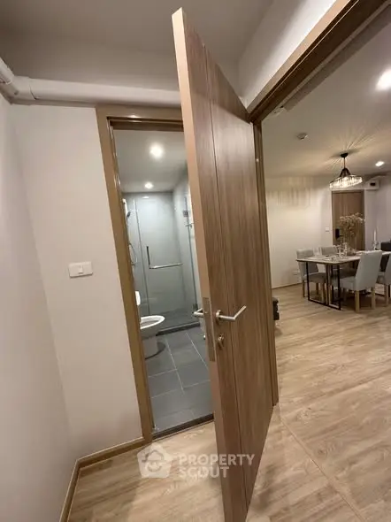 Modern apartment interior with open bathroom door and dining area view.