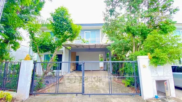 Charming two-story house with lush greenery and gated driveway, perfect for family living.