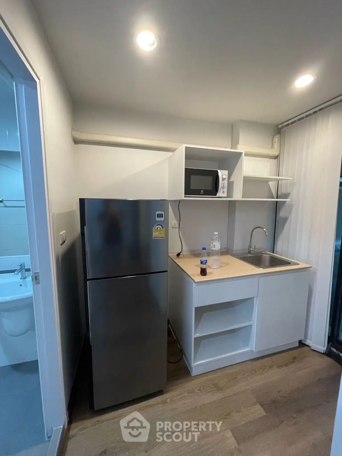 Compact kitchen with stainless steel fridge, microwave, and sink in modern apartment.