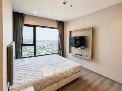 Modern bedroom with large window offering stunning city view, featuring a mounted TV and minimalist decor.