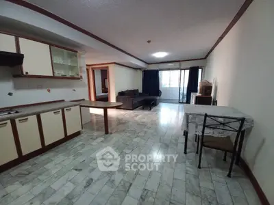 Spacious open-layout living room with kitchen and dining area, featuring tiled flooring and natural light.