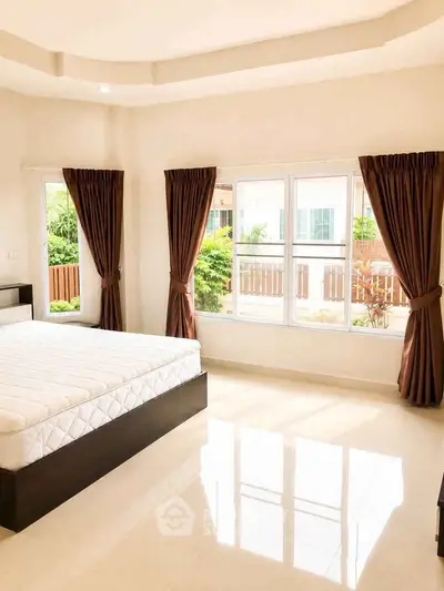 Spacious bedroom with large windows and elegant curtains, offering abundant natural light and a serene view.