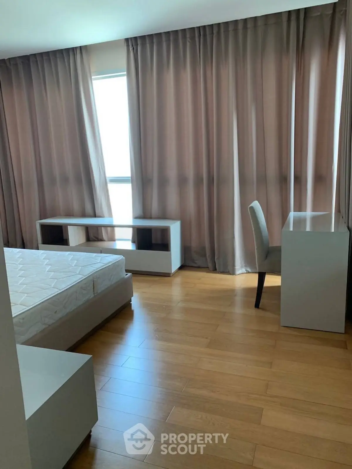 Spacious bedroom with wooden flooring and large windows for natural light.