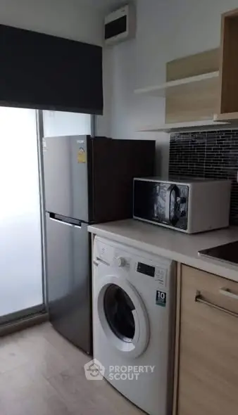 Modern kitchen with fridge, washing machine, and microwave in compact layout.