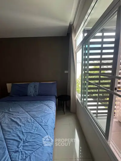 Modern bedroom with large window and blue bedding, offering natural light and a cozy atmosphere.
