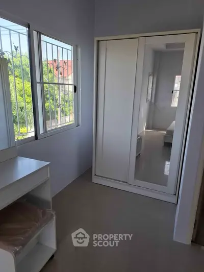 Bright bedroom with large windows and mirrored wardrobe, offering a serene view of lush greenery.