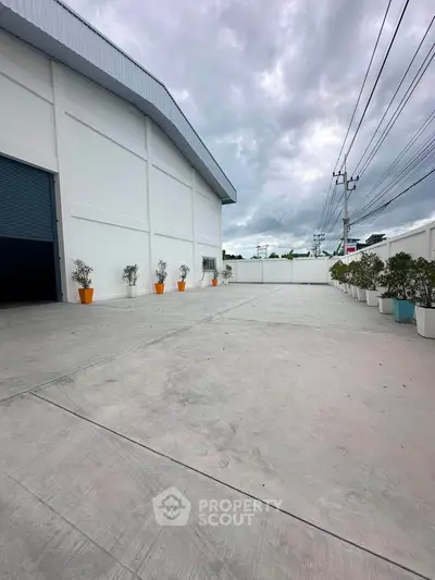 Spacious industrial warehouse exterior with ample concrete driveway and potted plants.