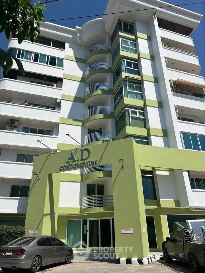 Modern condominium building with green accents and multiple balconies under clear blue sky.