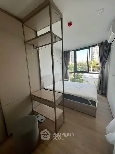 Modern bedroom with large windows and stylish shelving unit in a bright apartment.