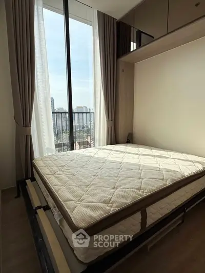 Modern bedroom with large window and city view, featuring a comfortable mattress and elegant curtains.
