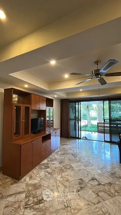 Spacious living room with marble flooring and ceiling fan, overlooking lush garden view.
