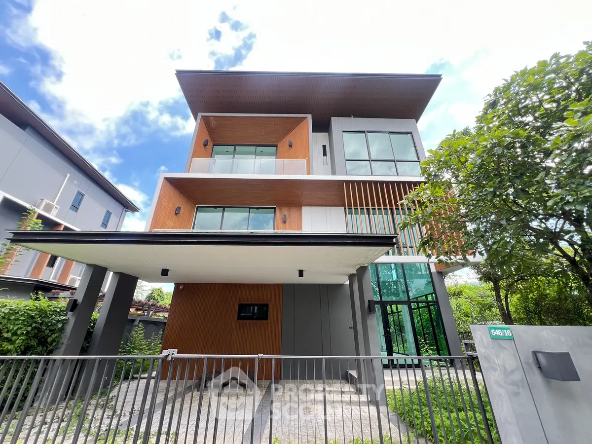 Modern three-story house with large windows and stylish facade in a lush green setting.