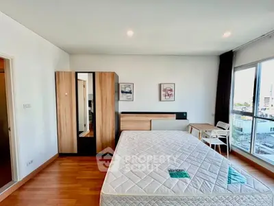 Spacious bedroom with large windows and modern furnishings in a city apartment.