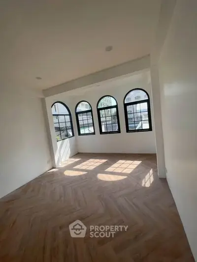Spacious room with elegant arched windows and wooden flooring, perfect for modern living.