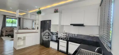 Modern open-layout kitchen with sleek white cabinets and black appliances, adjacent to a cozy living area.