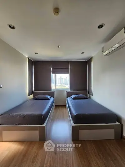 Modern bedroom with twin beds and city view, featuring sleek design and ample natural light.