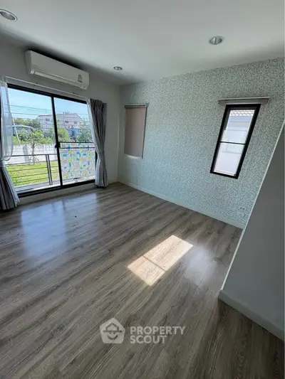 Spacious empty room with large window and air conditioning, featuring modern wood flooring and stylish wallpaper.