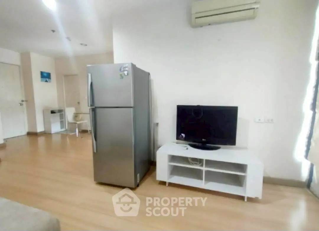 Modern living room with fridge and TV, featuring wooden flooring and air conditioning.