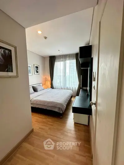 Cozy bedroom with modern decor and large window offering natural light.