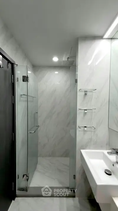 Modern bathroom with glass shower and sleek white sink in a contemporary apartment.