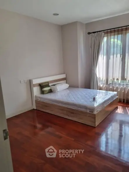 Spacious bedroom with wooden flooring and large window for natural light.