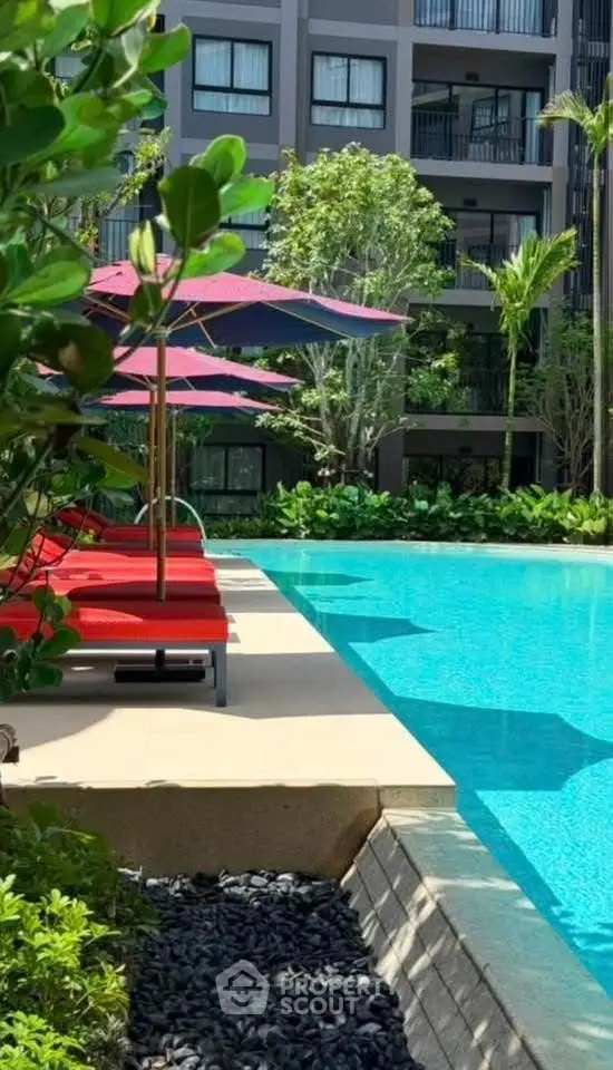 Luxurious poolside view with red loungers and lush greenery in modern apartment complex.