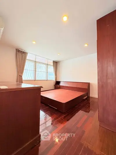 Spacious bedroom with wooden flooring and large windows for natural light.