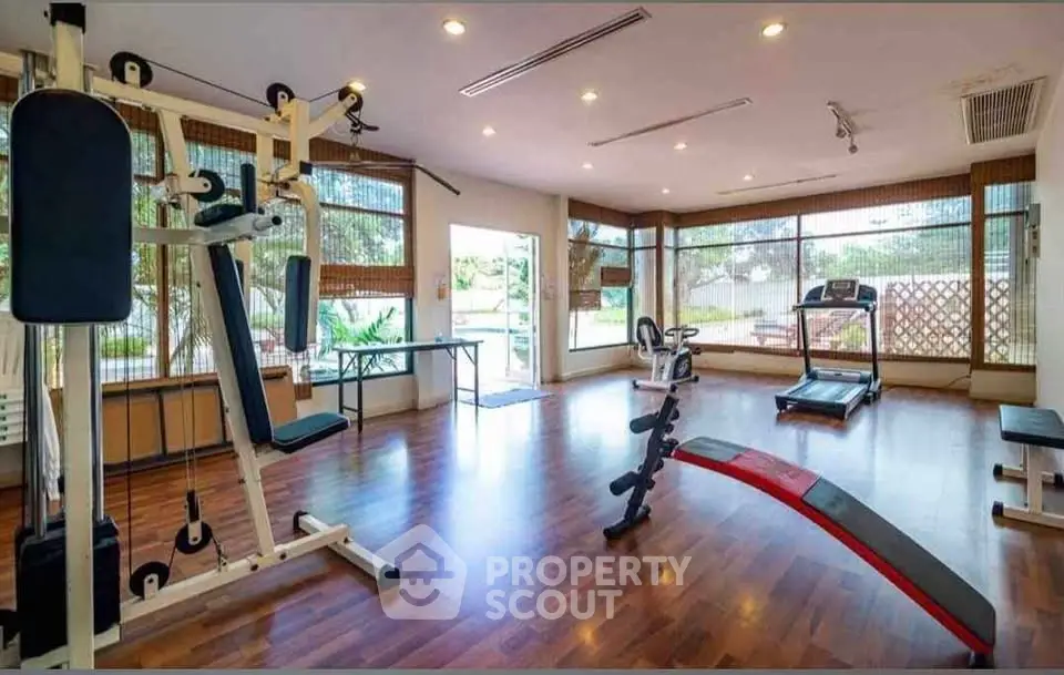 Spacious gym with modern equipment and large windows offering natural light.