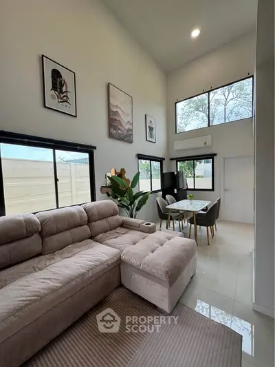 Spacious modern living room with high ceilings and large windows, featuring a cozy sectional sofa and elegant dining area.
