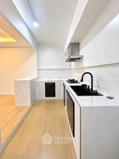 Modern kitchen with sleek white cabinetry and marble countertops, featuring a gas stove and open layout.