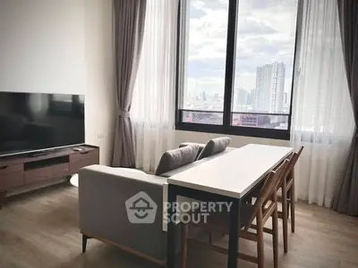 Modern living room with large windows and city view, featuring sleek furniture and natural light.