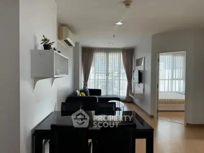 Modern open-plan living room with dining area and bedroom view, featuring sleek furniture and natural light.