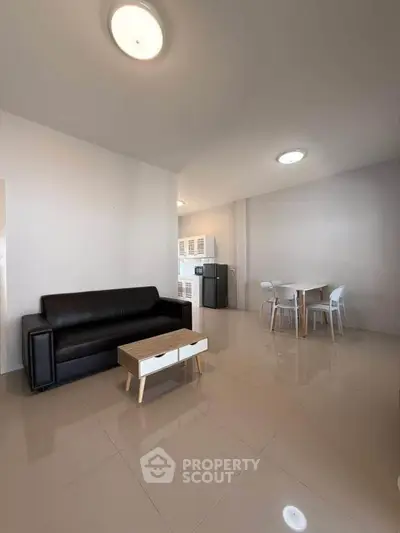 Spacious living room with modern furniture and dining area, featuring sleek black sofa and stylish table.