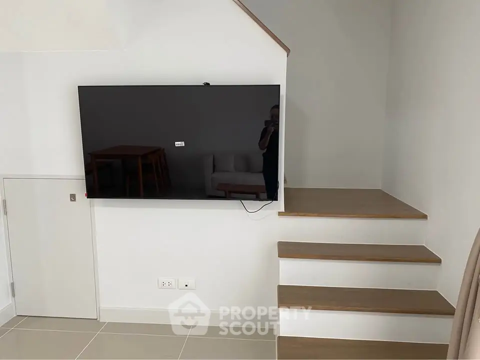 Modern interior with wall-mounted TV and wooden staircase in a stylish living space.