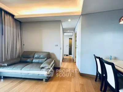 Modern living room with sleek leather sofa and elegant dining area, featuring warm wooden flooring and soft lighting.