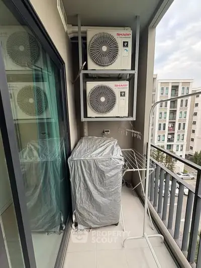 Compact balcony with air conditioning units and laundry drying rack in modern apartment building.