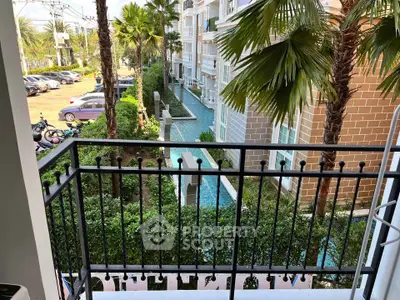 Charming balcony view overlooking lush garden and serene water feature in modern residential complex.