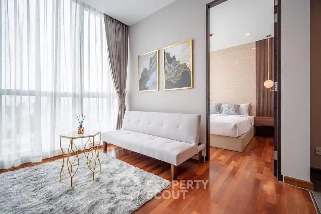 Modern living room with elegant decor and natural light leading to a cozy bedroom.