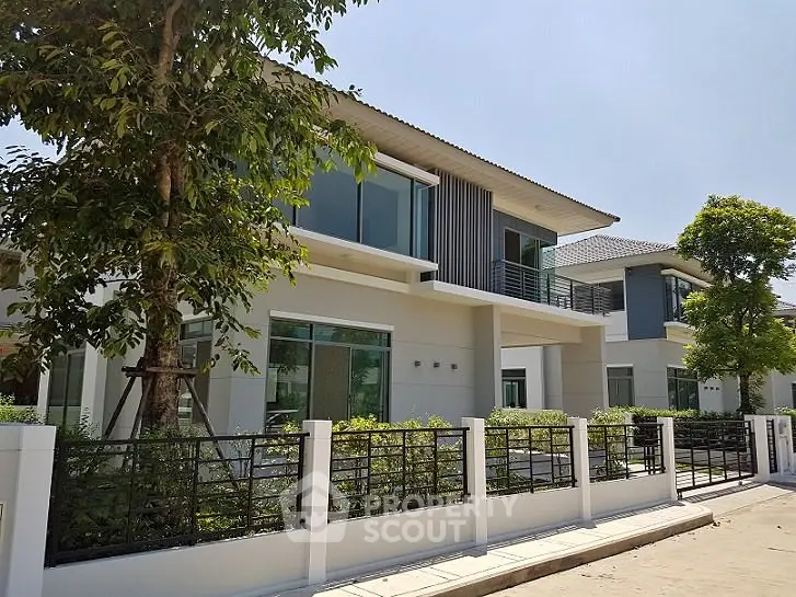 Modern two-story house with large windows and landscaped garden in a serene neighborhood.