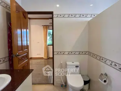 Spacious bathroom with modern fixtures and open doorway to a bright room with large window.