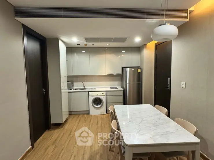 Modern kitchen with dining table, washing machine, and fridge in sleek apartment.