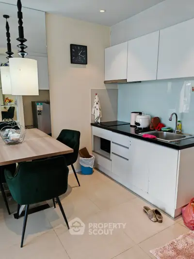 Modern kitchen with sleek white cabinets and dining area, featuring elegant green chairs and contemporary lighting.