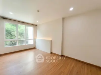 Spacious empty room with large window and wooden flooring, perfect for customization.